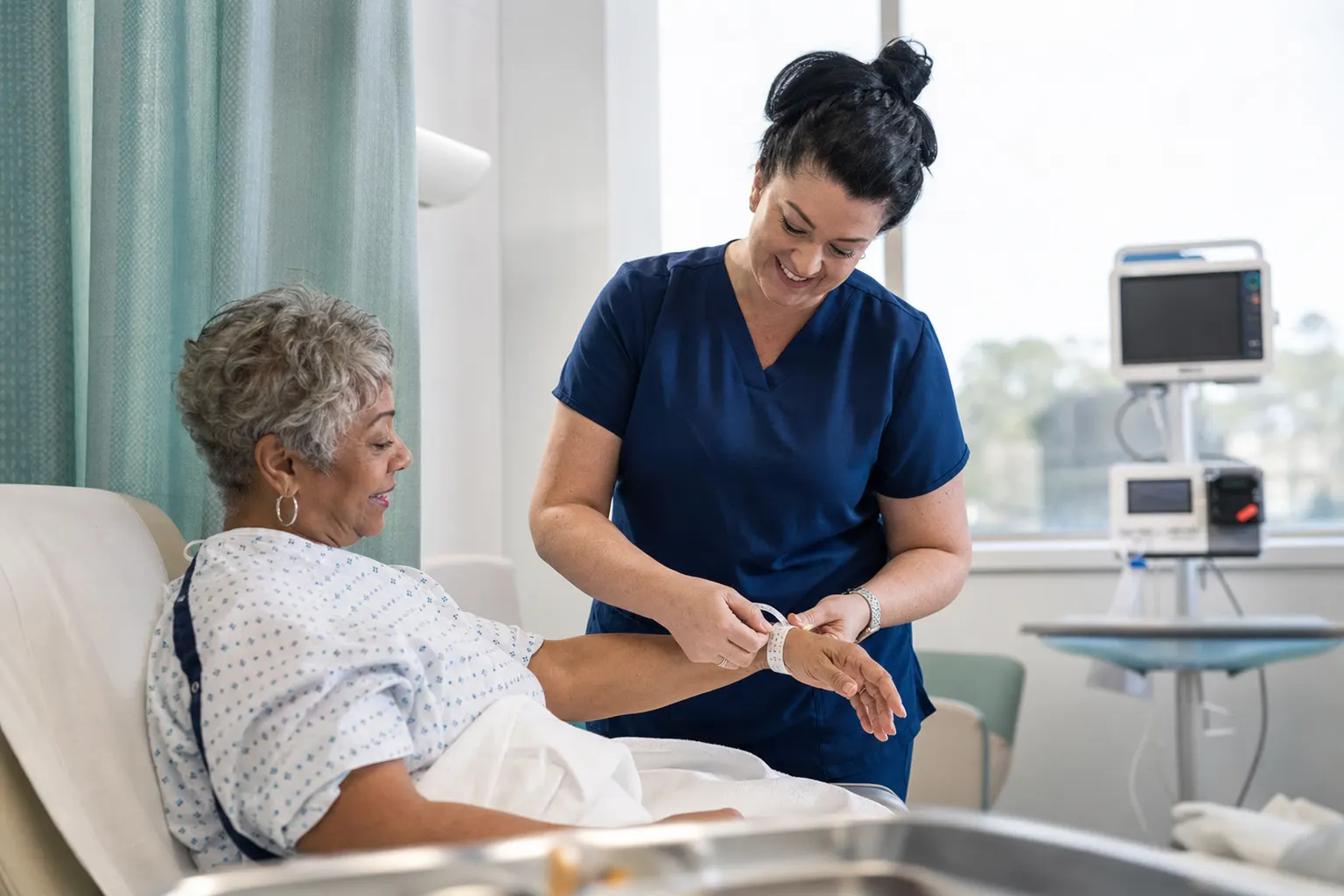 A nurse checking a patient's wristband in a private pre-operative bay